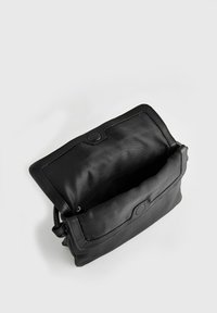 Bolso negro hecho de cuero y tela, con cierre de solapa, bolsillo interno con cremallera y textura suave. Vista abierta que muestra un compartimento espacioso.