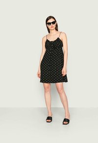Vestido preto de alças finas com padrão floral, fecho frontal de botões e detalhe de busto franzido. Combinado com sandálias pretas de slide e óculos de sol.
