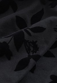 Tissu gris foncé avec un motif floral en velours noir doux montrant des feuilles et de petites fleurs en gros plan.