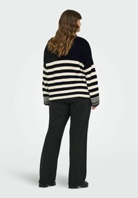 Zwart-wit gestreepte trui met een losse pasvorm en geribbelde manchetten, gecombineerd met zwarte wijde broek en stevige zwarte schoenen.