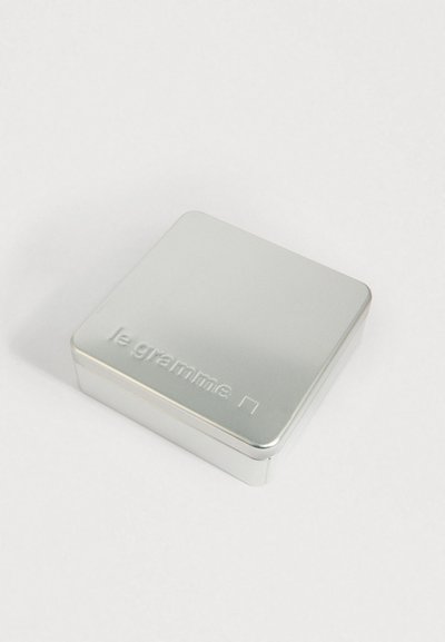 Mala srebrna metalna limenka s natpisom "le gramme" utisnutim na poklopcu, postavljena na jednostavnu bijelu pozadinu.