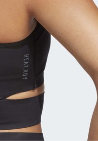 Černá sportovní podprsenka s přiléhavým střihem, měkkou tkaninou a výřezem. Obsahuje text "HEAT.RDY" podél bočního švu.