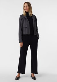 Szara krótka kurtka z zatrzaskami i dwiema przednimi kieszeniami, czarny golf, czarne spodnie o szerokich nogawkach oraz czarne loafersy. Gładka tekstura.