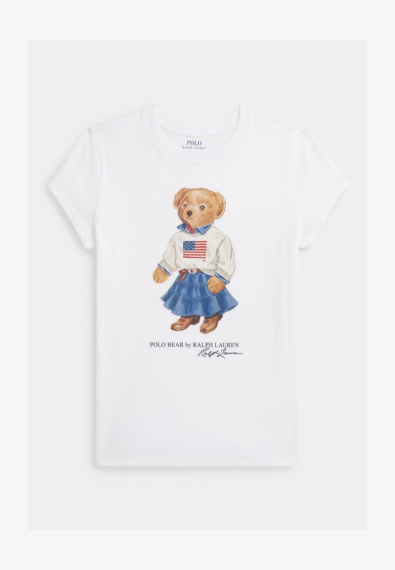 Balta medvilninė marškinėlių su animaciniu lokiu, kuris vilki megztinį su amerikietiška vėliava, džinsinę sijoną ir rudus batus, su tekstu "Polo Bear" žemiau.