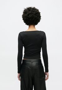 Top noir à manches longues avec un décolleté carré, coupe ajustée et texture lisse, associé à un pantalon en cuir noir taille haute avec poches.