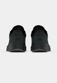 Μαύρα αθλητικά παπούτσια Nike με λείο πάνω μέρος με υφή σουέτ, στοιχεία από δίχτυ και χοντρή ελαστική σόλα. Το λογότυπο είναι ορατό στη φτέρνα.