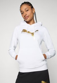 Sweat-shirt à capuche blanc avec le logo Puma doré, doté d'une poche kangourou et de bords côtelés, fabriqué en tissu doux et texturé.