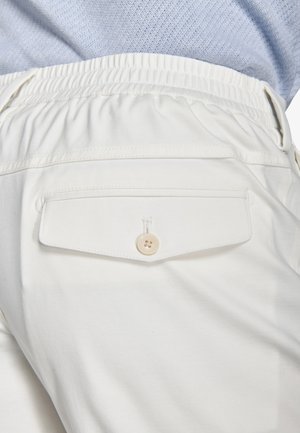 Hvide bukser med elastisk taljebånd og en knaplukket baglomme båret med en lyseblå tekstureret top.