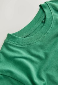 Zöld pamut póló kerek nyakkal és rövid ujjakkal. Az anyag sima textúrájú, látható varrási részletekkel.