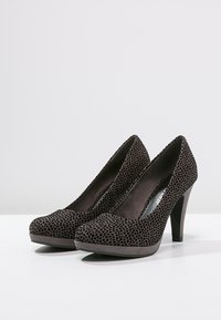 Escarpins en suède noir à talons hauts avec un bout rond, présentant une surface texturée de petites perforations et un talon de hauteur moyenne.