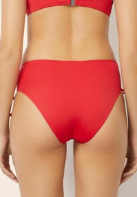 Chiloți de bikini roșii cu tăieturi înalte pe laterale, design fără cusături și textură de țesătură moale. Prezintă accente cu șnur la șolduri.
