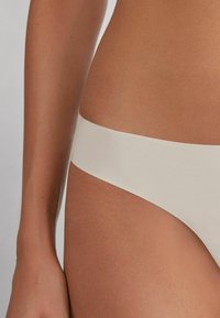 Białe majtki bikini o gładkiej, matowej fakturze i szerokim boku, z minimalistycznym wzorem i bezszwowym wykończeniem.