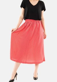 Falda midi a rayas rojas con cinturilla elástica, hecha de tejido ligero, combinada con una blusa negra de manga corta y tacones altos negros.