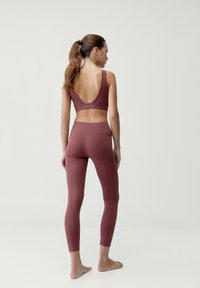 Športová podprsenka v melírovanej farbe s hlbokým V-zzadkom, doplnená o zladené legíny s vysokým pásom, ktoré majú detaily švov a hladký, elastický materiál.