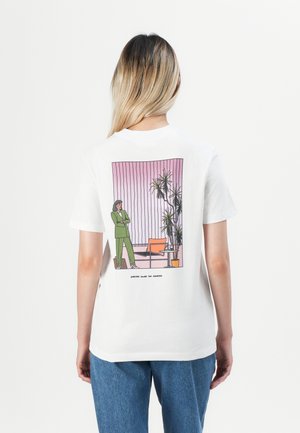 White cotton t-shirt featuring a colorful graphic on the back, depicting a figure in green attire with a plant and orange chair in a room setting.