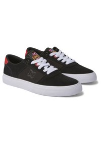 Schwarze Sneakers mit einem Obermaterial aus Wildleder und Stoff, weißen Schnürsenkeln, roten Akzenten an der Ferse und einer strukturierten weißen Gummisohle. Logo an der Seite.
