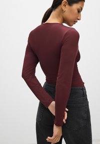 Bordeaux lange mouwen bodysuit, een aangesloten ontwerp, gladde textuur, met een ronde hals en sluiting aan de achterkant. Gecombineerd met zwarte high-waisted jeans.