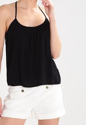 Top nero senza maniche con texture arricciata, scollatura rotonda e spalline sottili, abbinato a pantaloni corti bianchi con risvolti e piccoli bottoni metallici.
