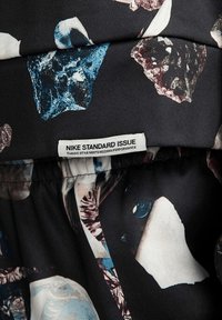 Tissu noir présentant un motif de pierres dispersées dans des bleus, des roses et des blancs. Comprend une étiquette blanche bien visible portant la mention "NIKE STANDARD ISSUE."