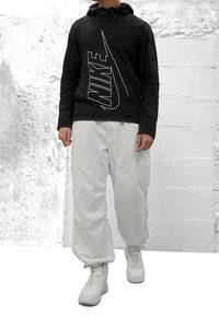 Sudadera negra con logo blanco de Nike, pantalones cargo blancos y zapatillas altas blancas. Tejido texturizado y detalle de capucha con cordón.
