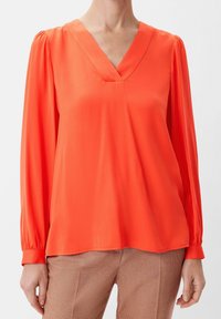 Blusa arancione brillante a maniche lunghe con scollatura a V. Tessuto leggero con una texture liscia, caratterizzata da dettagli arricciati sulle spalle.