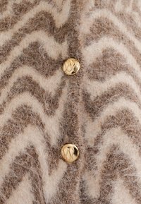Cardigan in lana a righe beige e marrone con una finitura morbida e texturizzata, dotato di bottoni tondi dorati su una pattina.