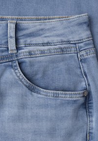 Lyseblå denimjeans tæt på, der viser forlomme, bæltestrop, gul syning og metalnitte detalje.