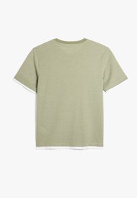 Lys grøn T-shirt med korte ærmer og rund hals, lavet af tekstureret stof. Har en hvid kantdetalje i bunden.