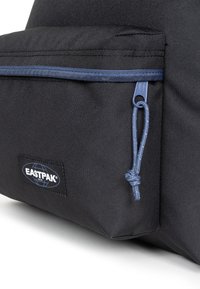 Zaino in tessuto nero con tasca frontale dotata di una cerniera blu e dettagli in corda, e una patch con logo Eastpak sul lato.