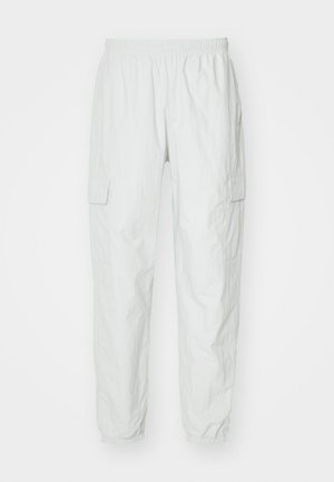 Pantalons cargo gris clair avec une taille élastique, dotés de deux poches latérales avec rabats et de poignets élastiques aux chevilles. Tissu texturé.