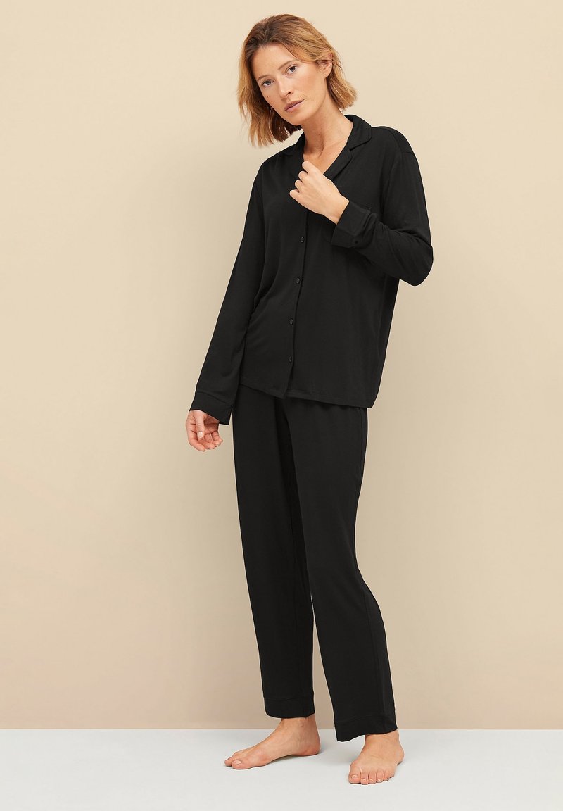 Zwart pyjama set met een knoopsluiting bovenkant met kraag en lange mouwen, gecombineerd met losse, rechte pijpen. Gladde textuur.