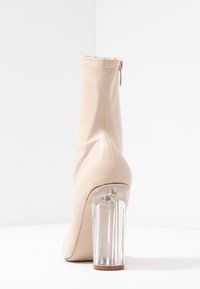 Beige leather ankle boot with a smooth texture, a zipped back, and a clear acrylic block heel. Features clean lines and seamless construction.