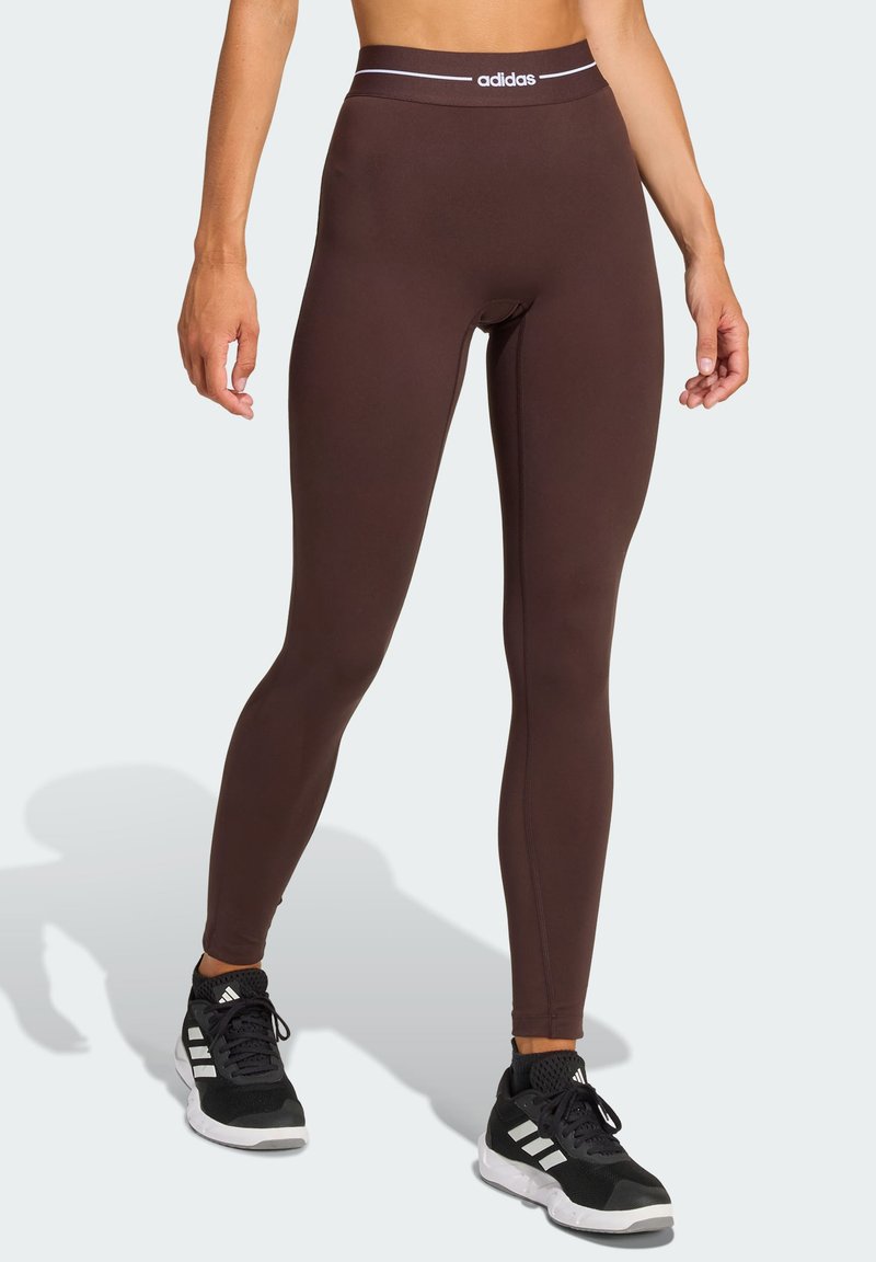 Brown leggings with a high waistband featuring a white adidas logo. Made from stretchy material, they have a fitted design and smooth texture.