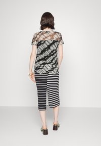 Top corto trasparente a maniche corte con motivo tie-dye in nero e beige, abbinato a una gonna a righe di lunghezza ginocchia in bianco e nero con uno spacco laterale.