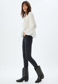 Blusa bianca strutturata con maniche ampie, abbinata a jeans neri slim-fit e stivali cowboy neri con ricami intricati.