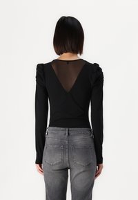 Black long-sleeve top features a V-shaped sheer back and puffed shoulders; paired with gray denim jeans with back pockets and a fitted shape.