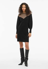 Abito nero con un accento marrone sulle spalle, caratterizzato da un scollo a V e maniche lunghe a sbuffo. Tessuto a maglia liscia.