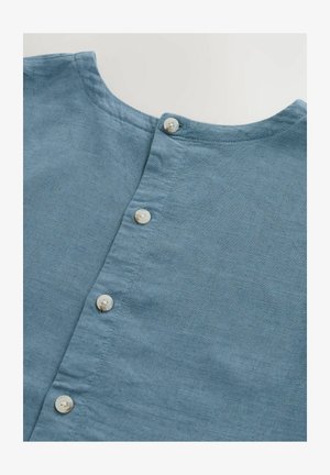 Jasnoniebieska lniana koszula z okrągłym dekoltem i sześcioma białymi guzikami z przodu. Gładka tekstura, widoczne subtelne detale splotu.