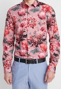 Bloemenprint overhemd met lange mouwen in tinten roze en rood met zwarte accenten. Heeft levendige bloemenpatronen en motdetails. Zwarte riem.