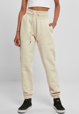 Lys beige joggebukser med elastisk høy midje, snøring, side lommer og ribbede mansjetter, sammen med svarte høye sneakers.