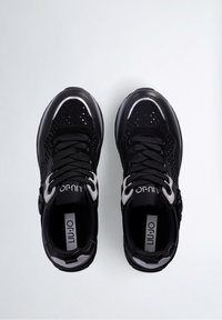 Zapatillas deportivas negras y plateadas reflectantes con cordones, diseño perforado y transpirable, y plantillas de marca sobre un fondo blanco liso.