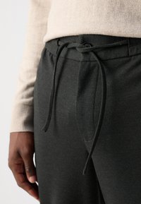 Pantalons en tissu doux gris foncé avec une taille élastique et un cordon de serrage. Comprend des poches latérales visibles et une coupe décontractée.