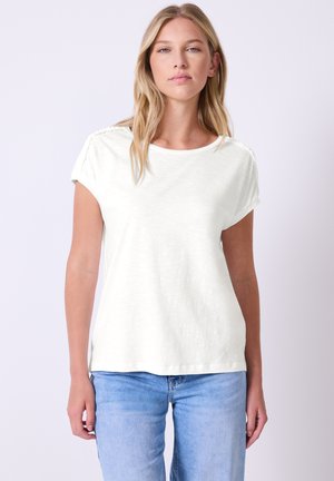 Hvid kortærmet t-shirt med en loose fit, der har teksturerede skulderdetaljer. Kombineret med lyseblå denim. Blødt, let stof.