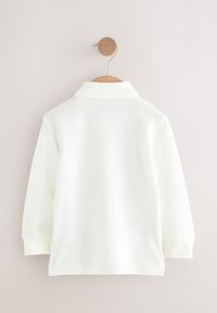 White long-sleeve polo shirt with a textured fabric, featuring a classic collar and a straight hem. Hangs from a wooden hanger.