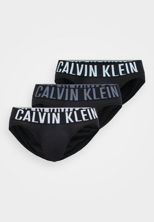 Trys juodų apatinio trikotažo poros su skirtingais juostos dizainais, ant kurių yra "CALVIN KLEIN" prekės ženklas kontrastingomis spalvomis. Lygus audinio tekstūra.