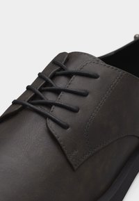 Κοντινό πλάνο σκούρου καφέ δερμάτινου υποδήματος με κορδόνια, λείο υφή και καθαρές ραφές κατά μήκος των πλευρών και των οφθαλμών.