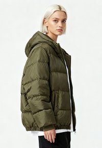 Doudoune vert olive avec capuche, présentant des coutures horizontales, un ourlet élastique et des poches devant. Fabriquée en matériau lisse et brillant.