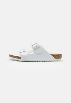 White slide sandal with two adjustable buckle straps, a cork footbed, and a textured rubber sole with a wave pattern.