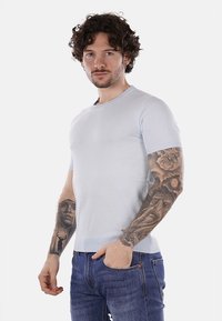 Maglione a maniche corte aderente di colore azzurro chiaro con scollatura a girocollo. Tessuto morbido, orlo a coste, indossato con jeans di colore blu scuro.