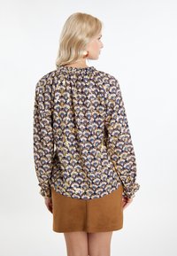 Blusa a fantasia floreale con scollatura arricciata, maniche lunghe e polsini elastici. Abbinata a una minigonna in suede marrone.